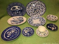 Full lot view showing 8 blue and white china plates of various sizes and patterns plus the white floral cup and saucer.