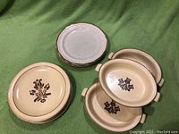 Photo showing four round Pfaltzgraff Baroque Japan plates and three oval serving dishes with a brown floral design on a creamy yellow stoneware base.