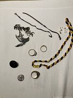Overview of all lot items on white background: coin, button, necklace, silver pieces, pearls, rings