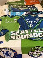 Photo displaying Seattle Sounders FC jerseys, scarves, hats, and flags arranged on a surface