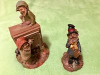 Two hand-carved painted wooden figures. One pair of figures on a rough wooden base; the other a single standing figure dressed in a top hat and holding an object.