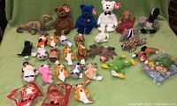 Full assortment of Ty Beanie Babies plush toys and mini beanies laying on green background including bears, penguins, frogs, and various other animals as well as two still packaged McDonald's Beanie Babies.