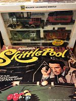 Photo showing the Aurora Skittle Pool game box with a man aiming a skittle ball and the train set box underneath
