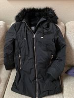 Front view of the black Zara Basic coat showing full length with zippered front and pockets, faux fur lined hood, and fitted sleeves.