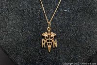 Close-up photo of the gold RN caduceus pendant on black background showing details.