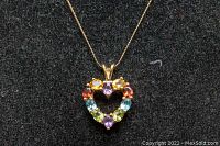 Close-up photo of the heart-shaped pendant showing multi-colored gemstones including amethyst, tourmaline, aquamarine and others set in 10K gold.