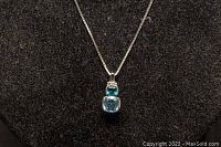 Front view of the pendant showing two blue gemstones, a smaller blue topaz on top and a larger aquamarine below, set in white gold.