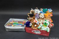 Photo showing over 15 Beanie Babies plush toys arranged in an open box, each plush with visible Ty tags attached.
