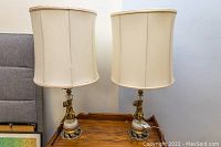 Pair of brass cherub table lamps shown together on wooden surface with cream shades.