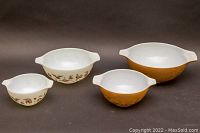 Four Pyrex nesting mixing bowls arranged showing white and brown versions with Americana farmhouse designs.