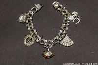 Full view of sterling silver charm bracelet with seven charms laid flat on a dark surface, highlighting the overall style and all charms.