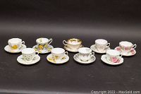 Front view of all nine teacup and saucer sets arranged together showing varied floral and gold designs