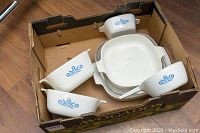 Box filled with 4 Blue Cornflower patterned CorningWare dishes with handles, showing various sizes and shapes in good composition, some with visible wear.