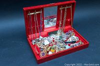 Jewelry box open showing necklaces hanging inside the lid and assorted necklaces, bracelets, and brooches loosely placed inside the box.