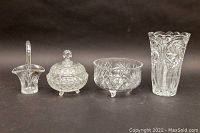 Four clear cut crystal items displayed on dark background: vase, covered candy bowl, footed fruit bowl, and Bohemian Czech basket with handle and sticker.