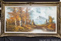 Full view of the large framed oil on canvas painting showing autumn landscape with trees, water, and mountain.