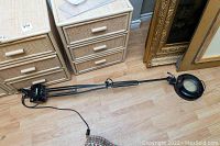 Full view of magnifying lamp with articulated arm laid on wooden floor, showing black circular lamp housing and clamp base.