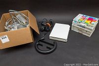 Photo showing white Nintendo Wii console, Wii nunchuck controller, black Wii Wheel accessory, power adapter and cables in a cardboard box, plus stack of 7 Wii game titles.