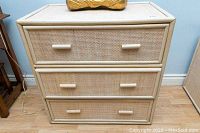 Front view of beige rattan and wood 3-drawer dresser showing drawer fronts and handles.