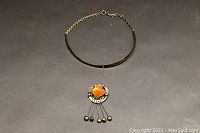 Silver plated choker necklace with orange agate pendant and dangling metal balls, laid flat on dark background.