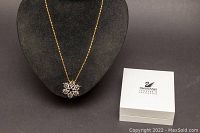 Full view of gold tone chain with snowflake pendant displayed on black bust stand and original Swarovski box beside it.