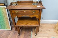 Full view of the Kaufmann wooden telephone/dressing table with single drawer and matching rolling seat under the table, showing the wood finish and brass handles.