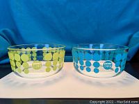 Two Pyrex anniversary bowls side by side showing the green and blue polka dot design and logos