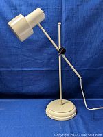 Desk lamp set against blue cloth background, showing front profile and adjustable arm and head.