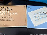 Two Inuit artist print reference books, one beige spiral-bound workbook, and one blue-covered book titled 'The Inuit Print'.