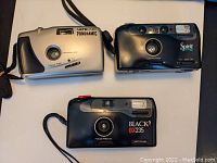 Three point and shoot cameras shown from the top view, displaying their lenses and control features.