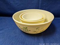 Nested set of three cream colored Pyrex mixing bowls with green floral vines, viewed from top and side to show size differences.