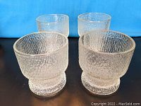 Four textured crystal old fashioned glasses seen from a slightly angled top-front view showing their shape and texture.