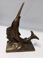 Front right angled view of the metal swordfish sculpture showing raised nose and detailed fins, base included.