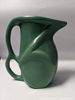 Front angled view showing the pitcher handle and spout with matte green finish and sculptural body detail.