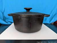 Front view of black cast iron pot with lid on, showing handles and lid knob