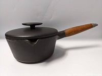Side view of the cast iron Copco pot with teak handle and lid on, showing the overall shape and handle detail.
