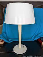 Front view of the lamp with the shade on, showing cream base and vertical stem with the white plastic shade.