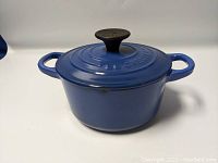 Side view of blue Le Creuset enamel cast iron pot with lid showing two handles and black knob.