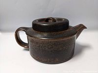Side view of dark brown mottled ceramic tea pot with lid and curved handle.
