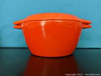Front view of the orange enameled Dutch oven with lid and side handles.