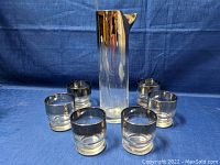 Full view of the Mid-Century Modern glass pitcher with six matching glasses arranged around it on a blue fabric background.