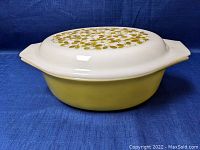 Front view of the Pyrex casserole dish showing olive green exterior and white lid with gold and white floral pattern.