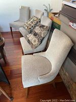 Angled group view of four beige upholstered chairs in a room, two with decorative cushions.