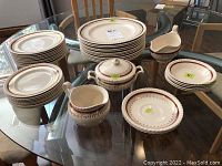 Full set arranged on glass table showing plates, sauce boat, creamer, and sugar bowl.