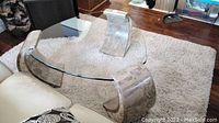Overview of glass coffee table with curved stone bases on carpeted floor near couch.