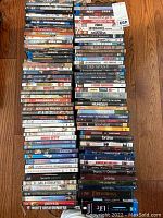Photo showing multiple stacks of DVDs and Blu-rays laid on a wooden floor, titles visible include thrillers, comedies, dramas.