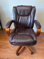 Front view of chair showing contoured high back, seat cushion and curved wood armrests