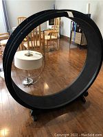 Front angled view of entire black exercise wheel with metal support base and casters in living area