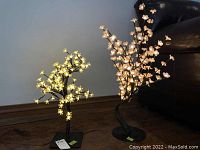 Two illuminated floral tree lamps showing warm LED flower lights on metal stems and round bases against a neutral background.