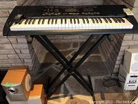 Full view of Casio CTK-3000 keyboard on black X-style stand with two external speakers and cables below.